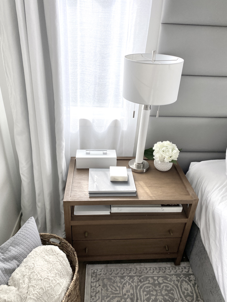masculine wood large nightstand dresser neutral tall bedside lamp styled side table blanket basket bedroom primary master bed decor white curtains window grey panel headboard