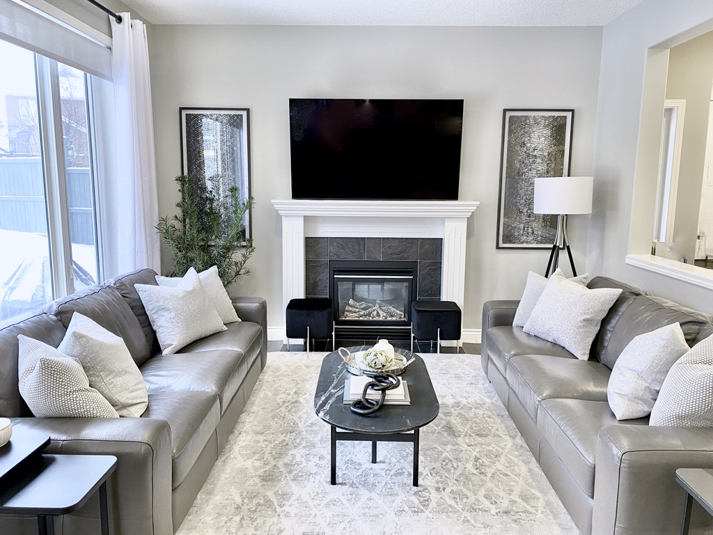 living room transitional contemporary grey leather sofas ottoman fireplace black and white gray grey velvet chain coffee table decor black marble oval tray styled styling chrome glam fireplace neutral geometric rug symmetrical small narrow matchin art pair large tripod lamp