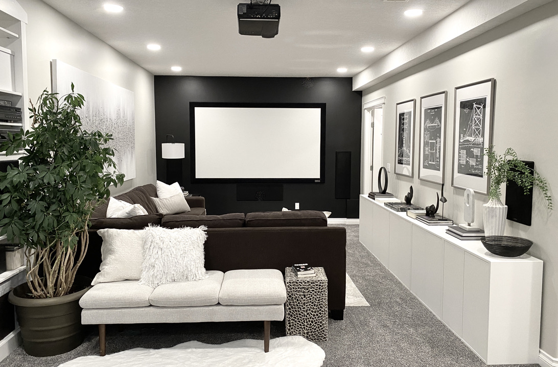 black theater wall movie room screen projector brown white cozy plants basement white storage cabinets games puzzles gallery wall pot lights long narrow room living room family room chocolate sectional grey gray