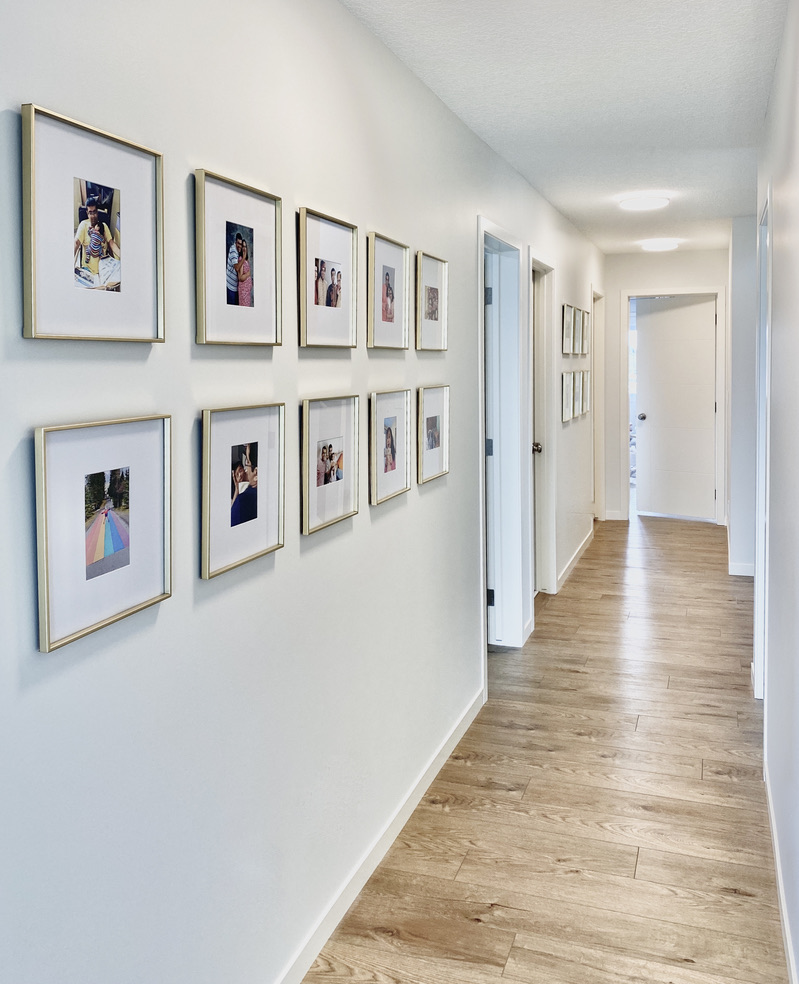 long hallway grid gallery wall square brass gold frames white mats family photos rows symmetrical