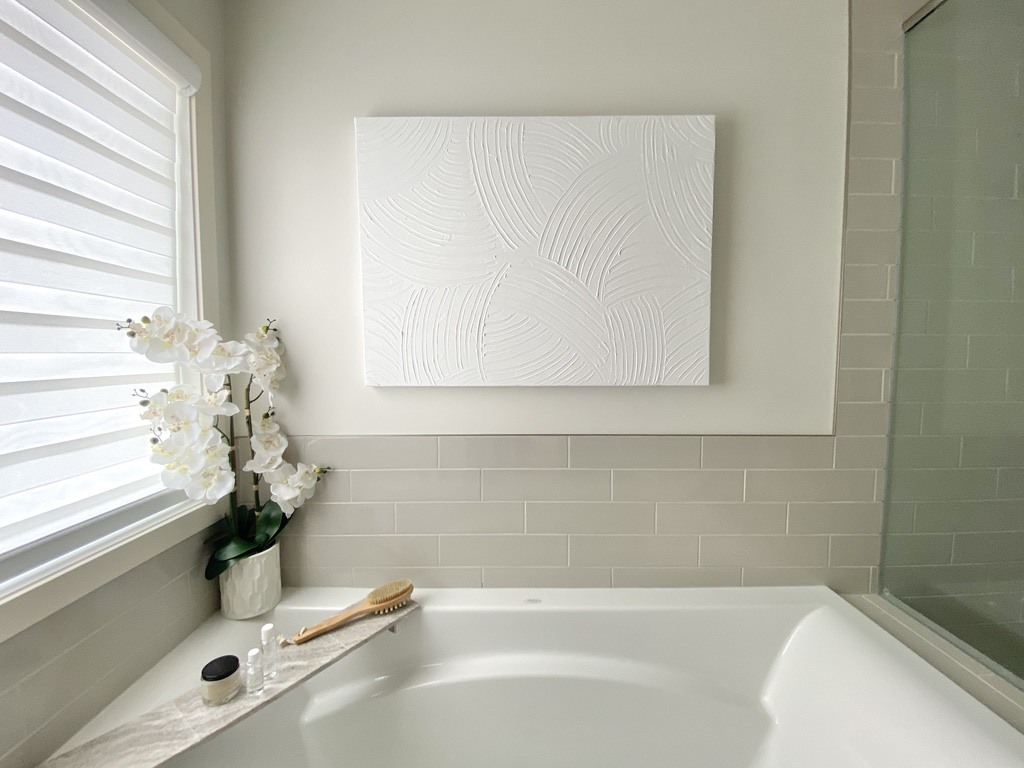 ensuite bathroom minimal simple space soft white grey beige ivory built in tub white wall art robe bathtub glassed in shower mosaic floor subway wall styled bath tray orchid