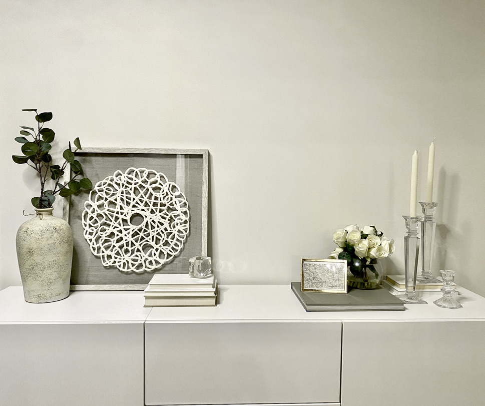white besta sideboard styled with soft neutral decor: glass candleholders, hardcover books, leaning paper machier art, beige stone textured vase and greenery, white roses, walls are painted benjamin moore white dove - calgary interior designer, bridgeland, Freya Home Interiors